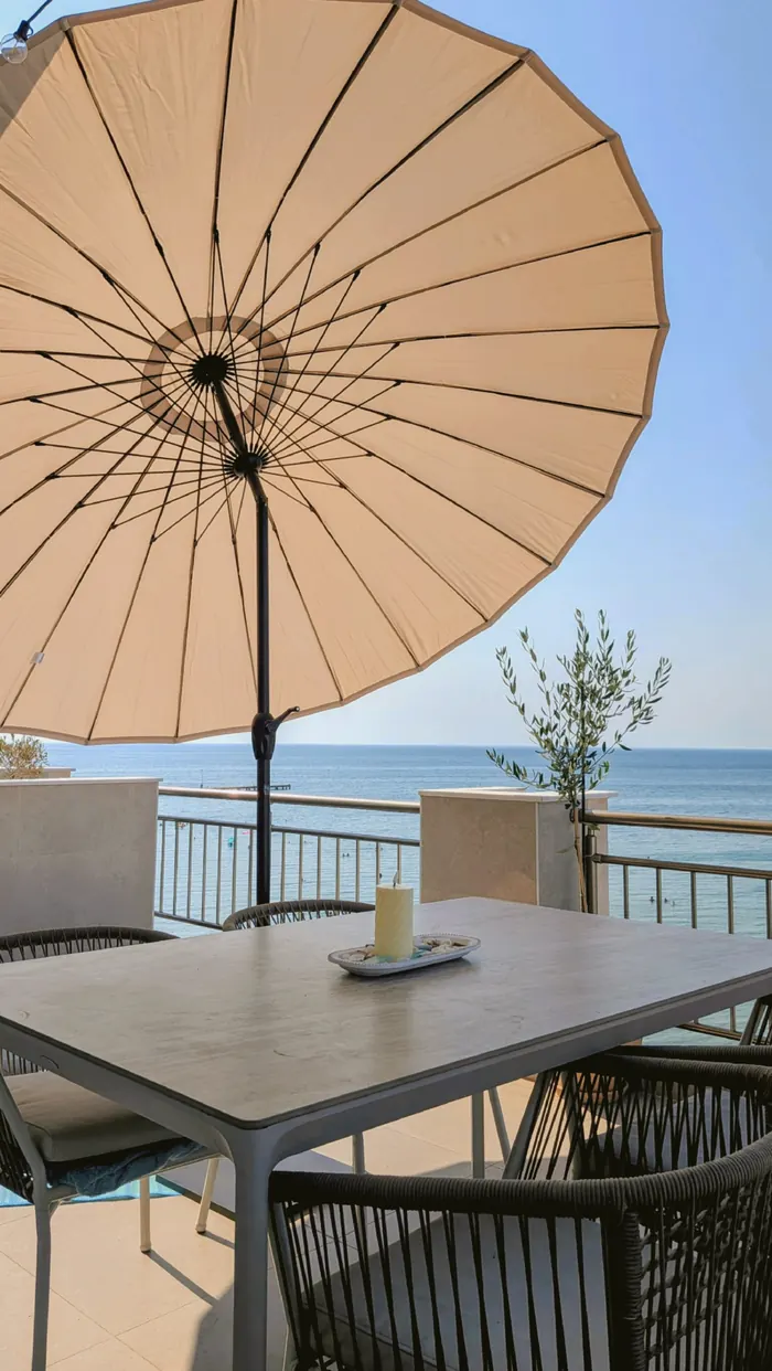 Shaded terrace table under a parasol, the sea beyond the railing